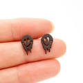 Close-up detail of gothic melted smiley face earrings in matte black stainless steel - Black