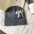 Detalle de gorro gris de punto con lazo blanco y textura de felpa sobre tela blanca - Gris