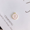 Macro shot of a pink round metal letter R pendant on a minimalist card background - Letter R