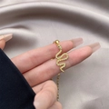 Dettaglio del ciondolo a serpente placcato oro 18K con zirconi su sfondo in raso grigio - 0625-Serpente a Forma di S Occhi Neri d'Oro