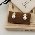 Detailed view of minimalist dual-size pearl earrings with gold metal bar on wood stand - Gold Large and Small Pearl Stud Earrings