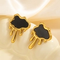 Detail van asymmetrische gouden oorknopjes met zwart emaille op een keramische schaal - Goud & Zwart