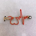 Close-up of golden stethoscope and heartbeat brooch with red enamel and crystal - EKG Black