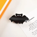 Chic black bat-shaped hair claw clip with white eyes on a vintage book background - Black Bat