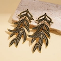 Detailopname van vintage gouden blad oorbellen met zwarte strass-steentjes op steen - Goud (Zwarte Strass)