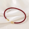 Macro shot of red braided rope bracelet with gold metal cylinder ends on silk background - True Red