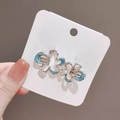 Hand holding silver floral hair clip with blue enamel detail on a white card display - Two Flowers Hair Clip