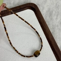 Detail of tiger eye bead necklace with a droplet pendant held over a wooden tray - 26# Irregular Rectangular Tiger Eye Necklace