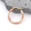 Macro detail of gold-plated bamboo hoop earrings with pink enamel beads on white stone - Khaki
