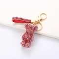 Detail of red rhinestone bear keychain with gold lobster clasp and ribbon on white pedestal - Red