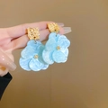 Détail de boucles d'oreilles fleur bleu clair avec métal doré et pétales de résine - Style Fleur Marbre Gaufré Or