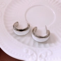 Dettaglio macro di orecchini a C in argento con smalto bianco su un piatto di ceramica - Argento-Bianco