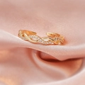 Macro detail of adjustable golden orbital ring with sparkling zircon inlays on pink silk - Gold Twisted/Cross Design