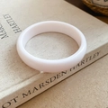 Close-up of a smooth white resin round bangle resting on a vintage art book - White