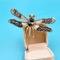 Dettaglio di una grande spilla a libellula con gemme nere e cristalli su sfondo blu - Nero