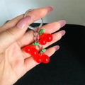 Close-up of translucent red resin cherry keychain with green leaves on black background - Red