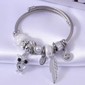 Silver twist rope charm bracelet with owl and feather pendants on white satin background - White