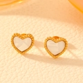 Primer plano de pendientes de corazón chapados en oro con incrustación de nácar blanco - Pendientes de botón de corazón