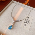 Macro detail of silver-tone teardrop zircon necklace on warm textured display - Blue Water Drop Style (Necklace-Blue Sancha)