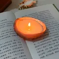 Macro detail of a lighted orange shell candle resting on an open book with warm lighting - Abalone Shell Candle [9-11cm] / Freesia [Bagged]