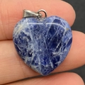 Blue heart-shaped natural stone pendant with white marble texture held between fingers - 20mm / Blue Sodalite