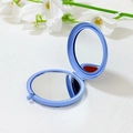 Close-up of light blue double-sided folding metal makeup mirror on a white surface - 65mm / Blue