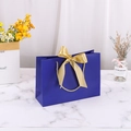 Dark blue paper gift bag with golden ribbon bow and gold rope handles on marble - Blue