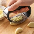 Manual stainless steel garlic press with black handle crushing cloves on a wooden board - Stainless Steel + Plastic / Arc Manual Garlic Press