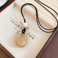 Close-up of beige teardrop acrylic pendant on black wax rope displayed in jewelry box - Beige