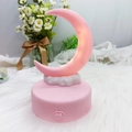 Macro detail of a pink crescent moon night light with a heart button on a white base - Pink