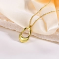Detalle de colgante dorado hueco irregular sobre piedra blanca y tela de seda color beige - Dorado