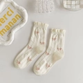 Close-up of white ruffled crew socks with pink bow patterns in a clean minimalist setting - Cream Bow Jacquard Ruffle