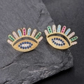 Golden evil eye safety pin earrings with colorful crystals on dark slate stone - Colorful