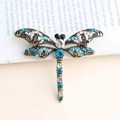 Spilla vintage a libellula con cristalli blu su bronzo davanti a una pagina di libro antico - Blu Pavone