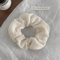 Detailed close-up of cream textured knitted hair scrunchie on elegant white tissue paper - Off-white