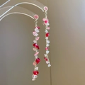 Detail of pink stone fringe earrings with gold chains on a clear display stand - Red Pink