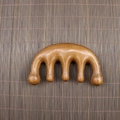 Close-up of five-tooth sandalwood scalp massager with natural wood grain on bamboo mat - Golden Sandalwood Small 5-Tooth Comb (9.5*5.5*2cm)