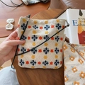 Detalle de bolso bandolera de lona bordada con motivos florales sobre una mesa de madera - Beige con bordado de flores azules amarillas y naranjas