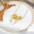 Macro shot of 18k gold plated bow pendant necklace on a decorative ceramic dish - Gold Polished Bowknot