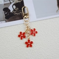 Golden keychain featuring red enamel flower pendants with a sturdy spring clasp - Red