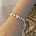 Detailopname van witte kralenarmband met gouden letter Z-bedel gedragen om de pols - Letter Z Stijl (Z)