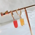 Macro shot of asymmetric gold earrings with red and orange cylindrical stone pendants - Red Agate