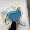 Détail du sac bandoulière cœur en cuir PU bleu tenu sur une veste de costume blanche - Bleu