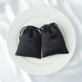 Pair of elegant black satin drawstring pouches for jewelry storage on white ceramic plate - Black