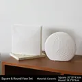 Minimalist white ceramic vase set with linear relief texture on wood furniture - A Set Of White Round And Square Ceramic Vases