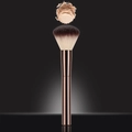 Rose gold makeup brush with brown bristles capturing loose powder particles - Powder Brush