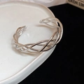 Macro view of silver woven open bangle with intricate twisted metal lines on ceramic plate - Silver Twisted Woven Style