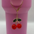 Detail of a cherry pendant with red resin fruit and green leaves on a golden chain - Red
