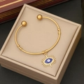 Detail of gold open bangle featuring a blue evil eye charm and ball accents - Royal Blue