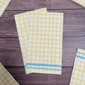 Folded paper napkins with yellow and white checkered pattern and blue wave trim - Yellow Check